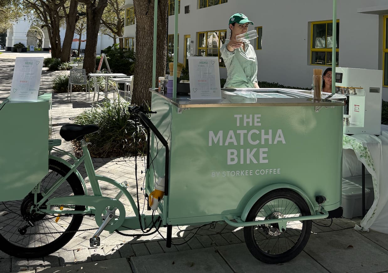 Side view of The Matcha Bike cart with barista pouring on a tree-lined Miami street